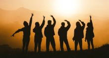 Silhouette of people celebrating with arms raised against a bright sun.